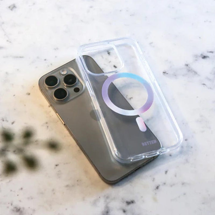 The Bryten by Raptic iPhone 15 MagFx MagSafe Case, featuring a transparent design with a circular pattern for drop protection, is placed on top of a silver smartphone lying on a white marble surface.