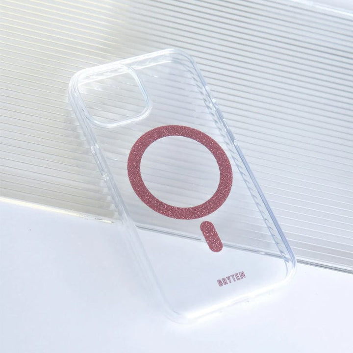 The Bryten by Raptic iPhone 15 MagFx MagSafe Case, featuring a clear design with a glittery pink ring and the word "Bryten" at the bottom, is compatible with wireless charging and placed on a white surface.