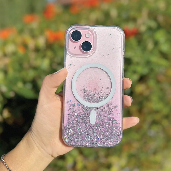 A hand holds a Bryten by Raptic iPhone 15 Series Starburst MagSafe Case with a glittery, star-filled, reflective iridescent design and a circle for seamless MagSafe integration against a blurred outdoor background.