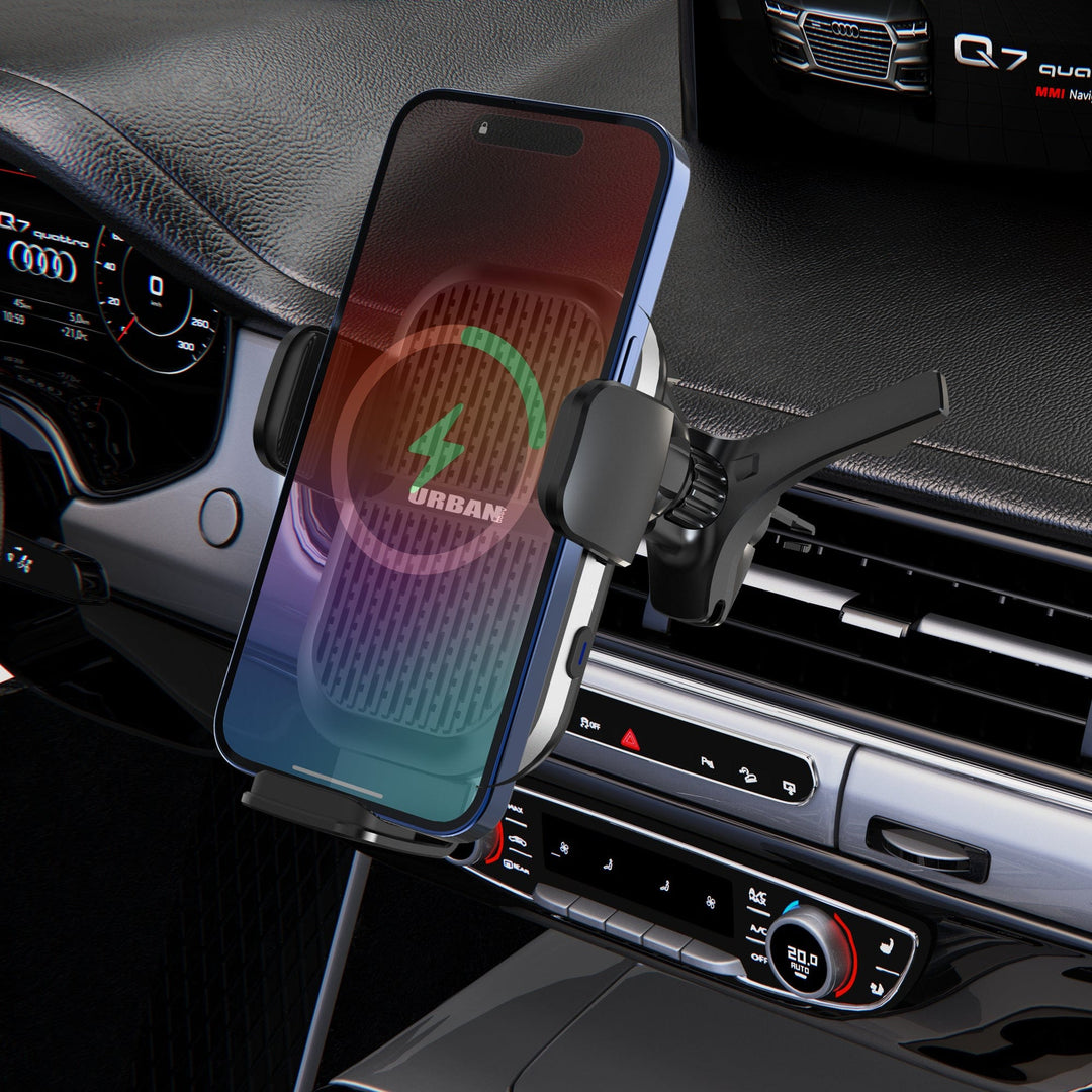 The Urban Wireless Cooling Car Charger - Auto15 Pro (Complete Kit) from Urban securely mounts a smartphone on a car air vent, with its screen showing the fast wireless charging icon. The dashboard and control panel of the car are visible in the background.