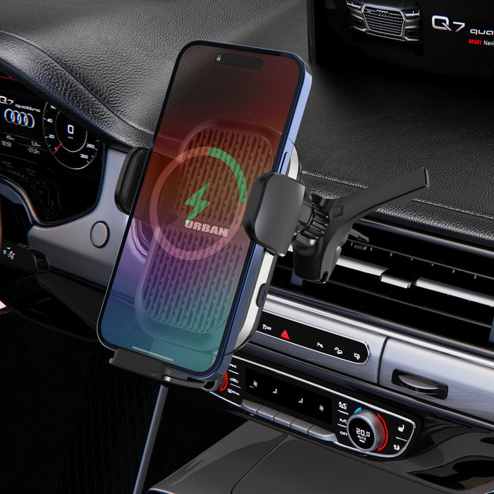 The Urban Wireless Cooling Car Charger - Auto15 Pro (Complete Kit) from Urban securely mounts a smartphone on a car air vent, with its screen showing the fast wireless charging icon. The dashboard and control panel of the car are visible in the background.