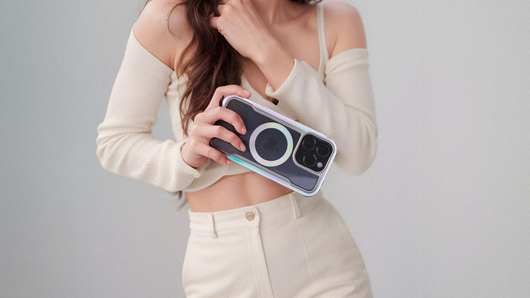 Hands holding a smartphone with a protective case, featuring a distinctive circular design on the back, and a dual-camera system.