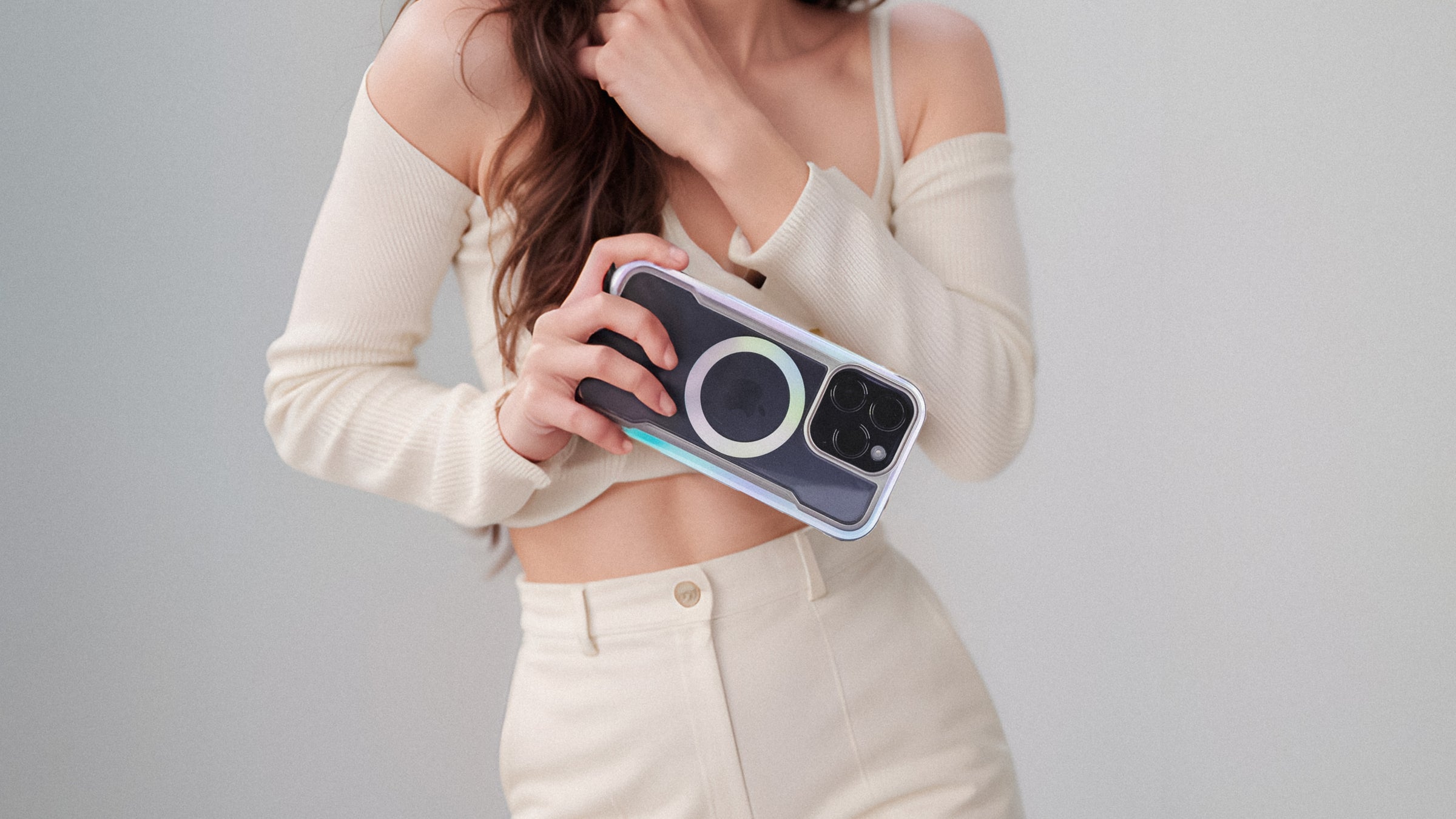 Hands holding a smartphone with a protective case, featuring a distinctive circular design on the back, and a dual-camera system.