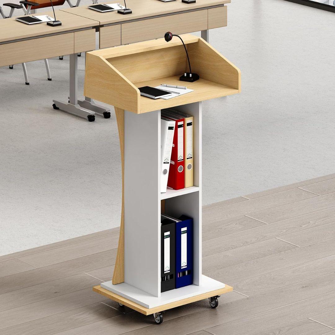 The MobileTechnica Podium Lecturn Rolling Stand features a spacious reading surface, built-in storage shelves for ring binders, and easily moves on wheels. Positioned in a bright room with desks and chairs, it’s ideal for lectures or speeches.