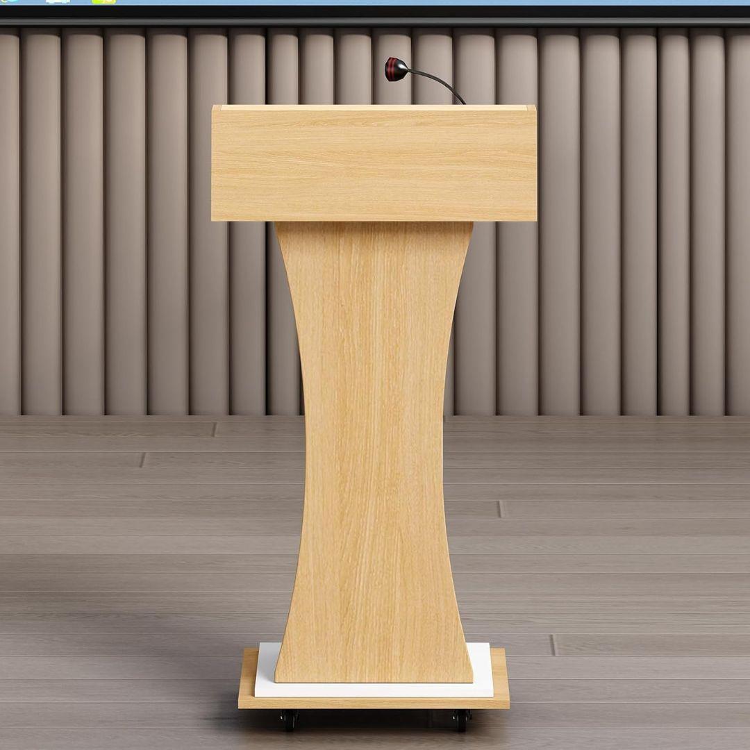 The MobileTechnica Podium Lecturn Rolling Stand, featuring a curved base, storage shelves, and a gooseneck microphone, stands on a light wood floor against vertical taupe wall panels. No people are present.
