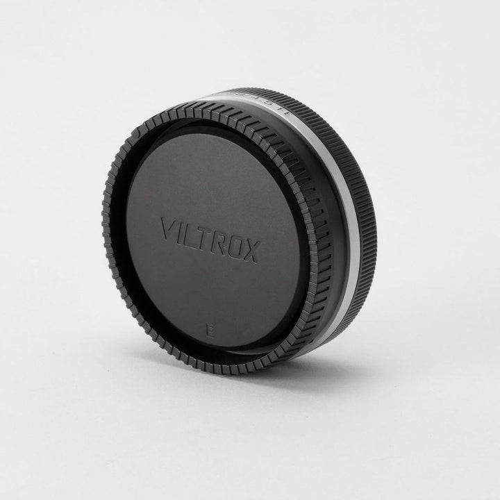 A black Viltrox lens cap for the Viltrox 28mm f/4.5 FE (Sony Full Frame) stands upright on a white background. The cap features a ridged edge for grip and "VILTROX" embossed in the center, with even lighting and soft shadows below.