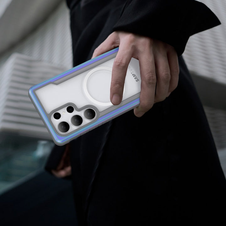 A person holds a Samsung S25 Shield Case - Raptic Shield with shock absorption and unique, partially transparent design featuring a large circular area for multiple camera cutouts. They're dressed in a dark jacket against an abstract, modern architectural background with diagonal lines.