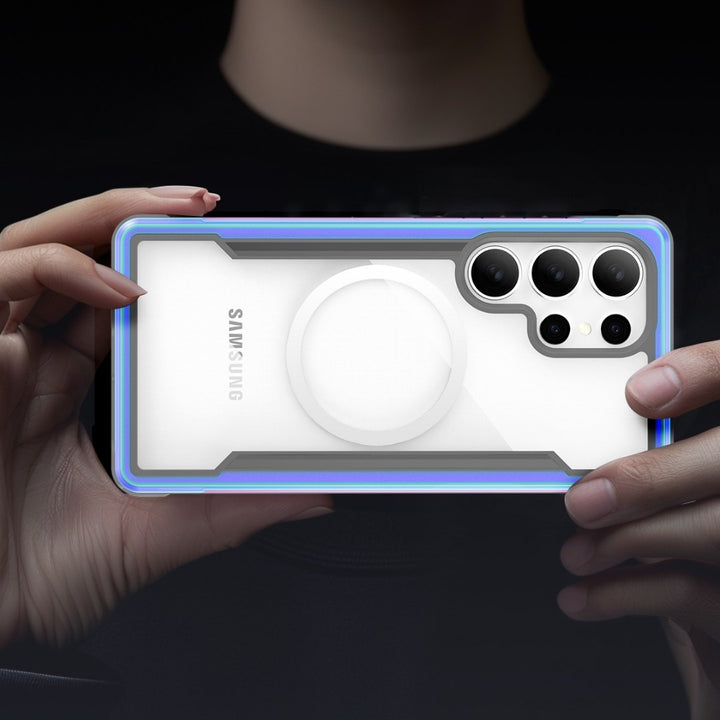 A person holds a smartphone horizontally, showcasing the Raptic's Samsung S25 Shield Case—transparent with blue edges and a white central circle design featuring the Samsung logo. It offers military-grade protection, encasing the camera module with three lenses and an LED flash against a dark background.