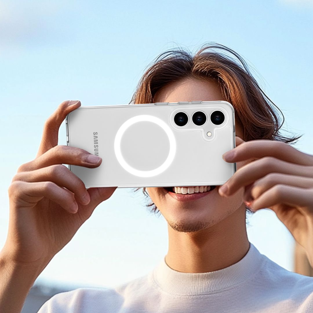 A person with shoulder-length brown hair holds a Raptic Crystal MagSafe case for the Samsung S25 Series, featuring drop protection. The sleek design is showcased against a clear blue sky as they smile in a white shirt.