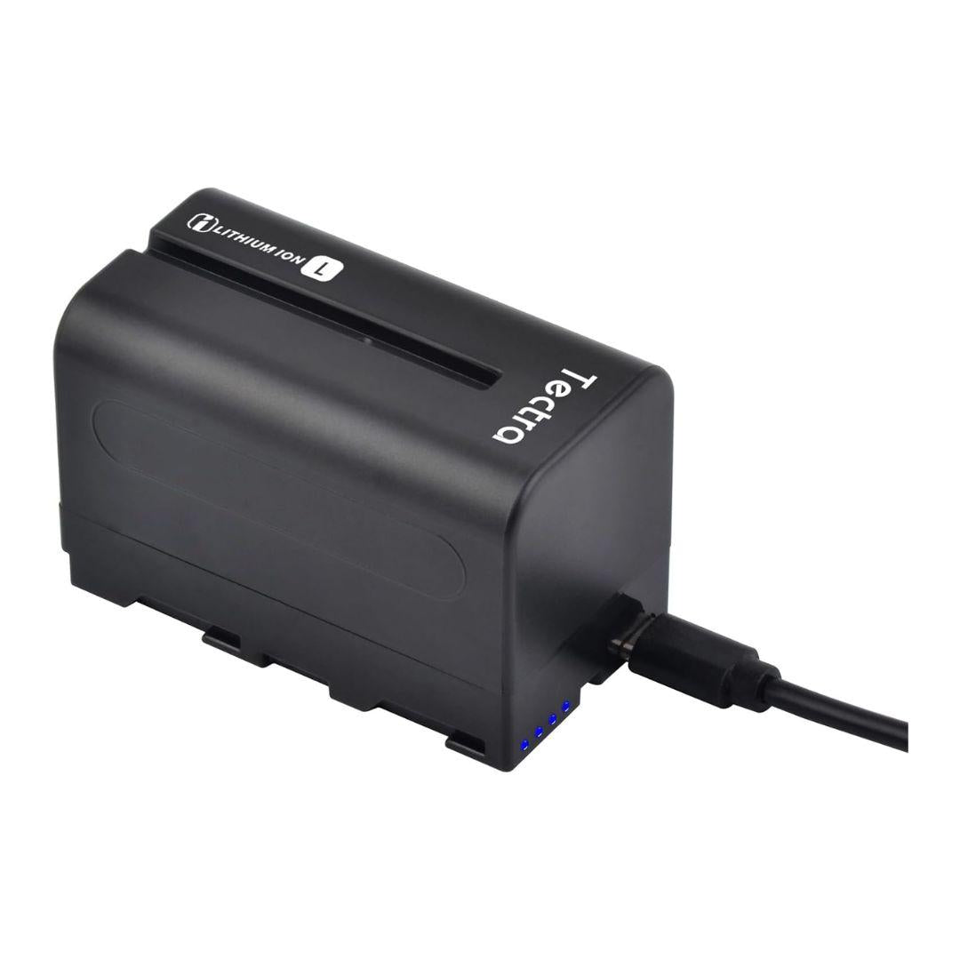 A MobileTechnica Tectra 6000mAh NP-F970/F750/F550 battery is inserted in a black charger labeled “for Sony NP-F series,” with a USB cable plugged into the side and four blue LEDs displaying charging status.