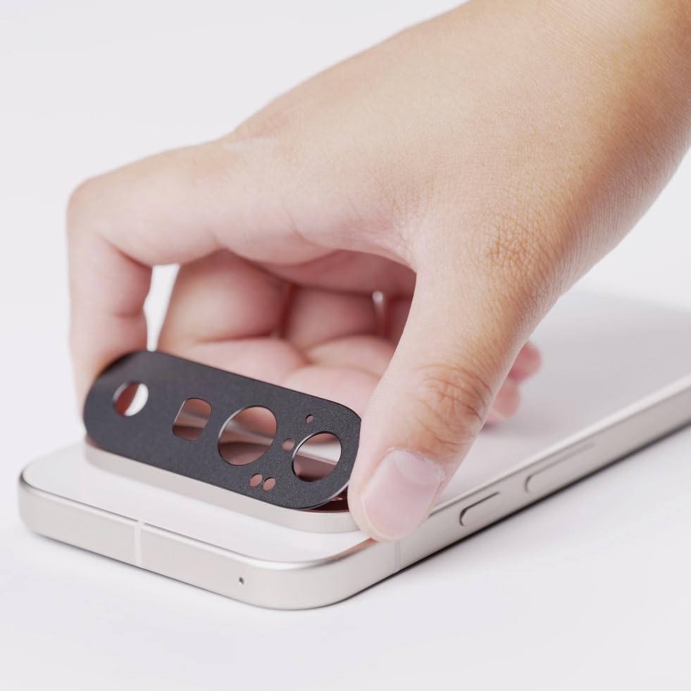 A hand holds the MobileTechnica Google Pixel 10 5G Camera Lens Protector above the rear camera of a silver phone, ready to apply. The phone, with a white surface and an aplus carousel container beside it, awaits the anti-scratch tempered glass.