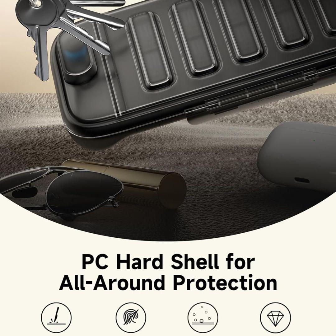 A black, ridged Nintendo Switch 2 Slim Carry Case by Jsaux is shown partly open with keys on top, highlighting its durable PC hard shell. Nearby are sunglasses and a cylinder. Icons for shock, fingerprints, dust, and drops appear below. Holds 10 game cards.