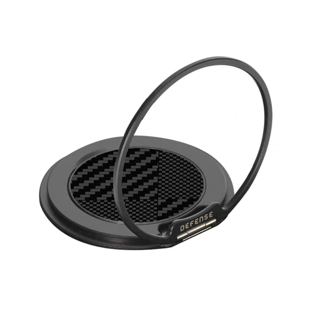 The MobileTechnica Magnetic Ring with Pop holder - Raptic Defeme is a round black 360° phone ring featuring a checkered carbon fiber center, "DEFENSE" on the ring, and serves as a sturdy kickstand when propped upright.