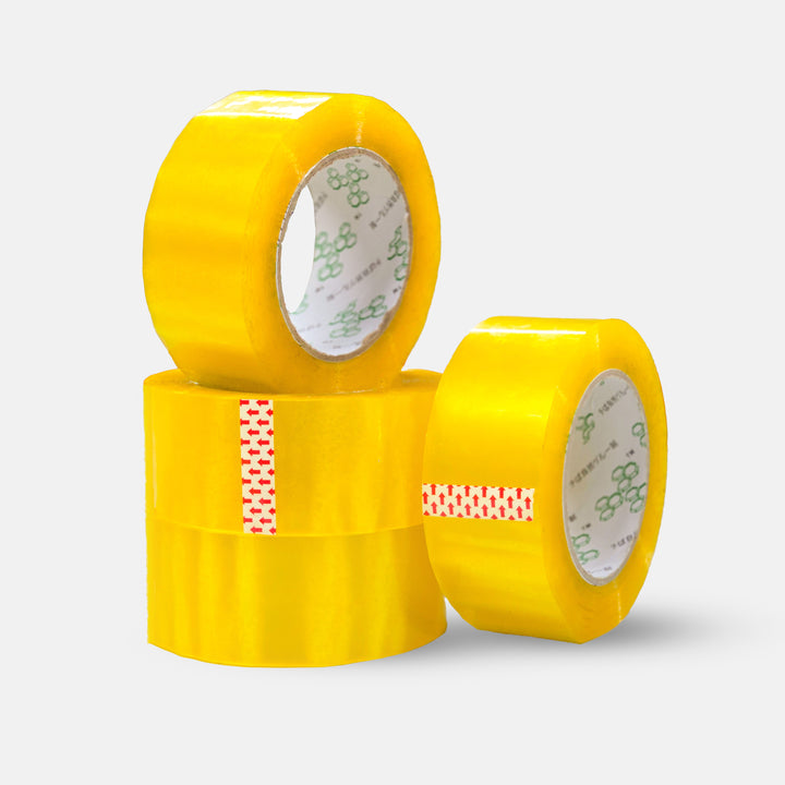 Four rolls of MobileTechnica Clear Packaging Tape are stacked on a neutral background. Two tall rolls stand behind one on top of another shorter roll in front. Each roll highlights strong adhesion and visible inner cores, with green symbols on one and red text on another.