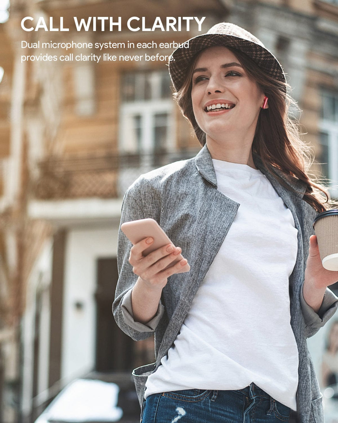 A woman with a hat and an Aukey MiniNC Active Noise Cancelling Earbuds listening to music while holding a smartphone and a cup of coffee