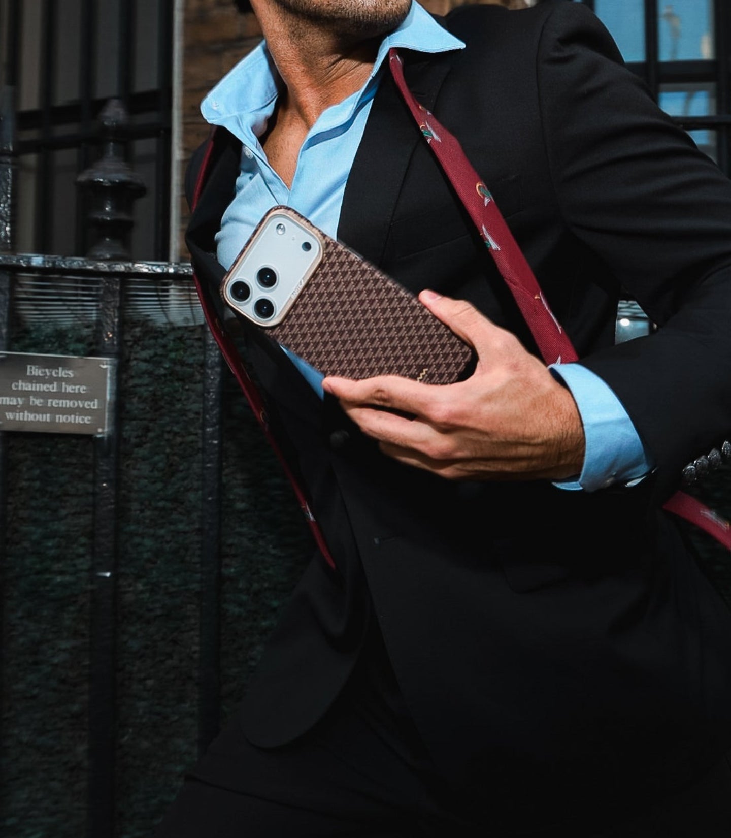 Man in a suit holding a brown textured bag with a phone case on a city street.
