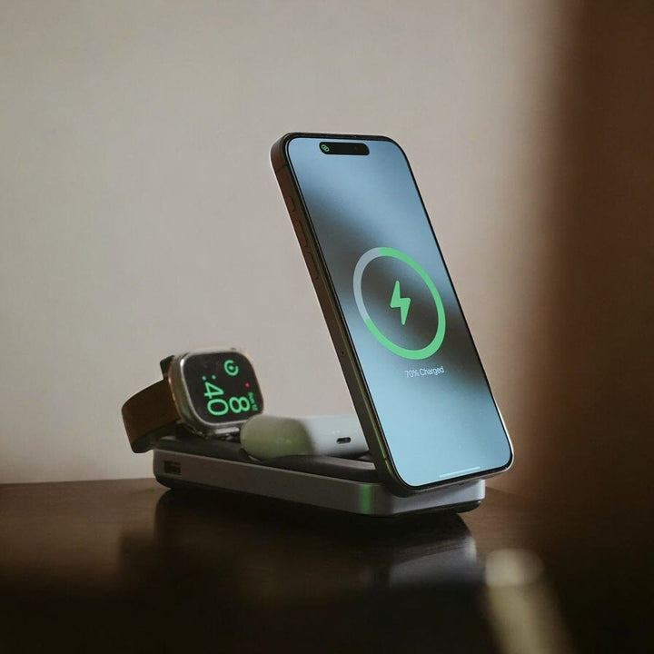 The **Urban PowerBuddy 5in1 Wireless MagSafe Powerbank 2** by **Urban** proudly displays a smartphone, smartwatch, and wireless earbuds on its travel-friendly charging pad. The phone, upright at 70% charge, shows a green lightning bolt icon. The smartwatch, lying flat, displays the time "4:00." The earbuds rest next to the devices on the sleek multi-device charging station.