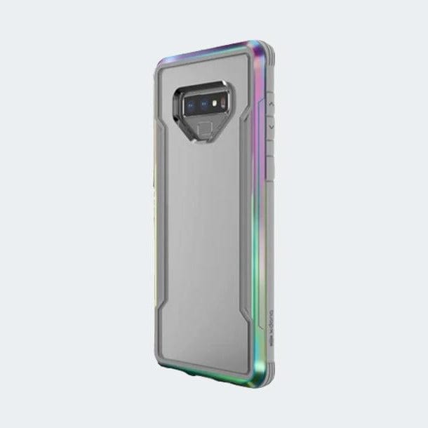 A Samsung Galaxy Note 9 equipped with the X-Doria Defense Shield case by Raptic. The grey, military-grade protective case showcases the phone's rear camera and buttons. It features a metallic finish with green and pink accents along its edges and supports wireless charging.